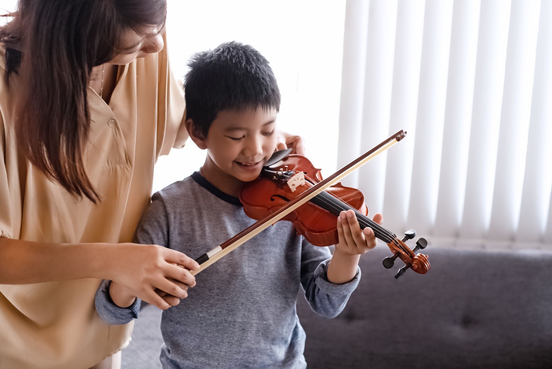 A woman is teaching a young boy how to play a violin.